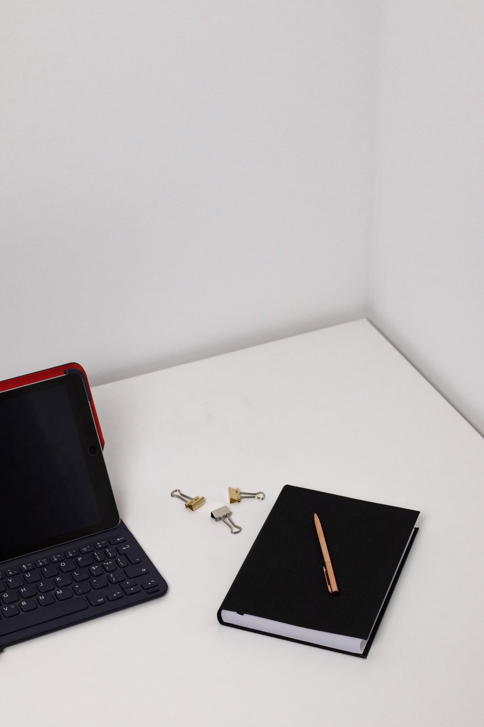 A clean workspace with a tablet, keyboard, notebook, and pen