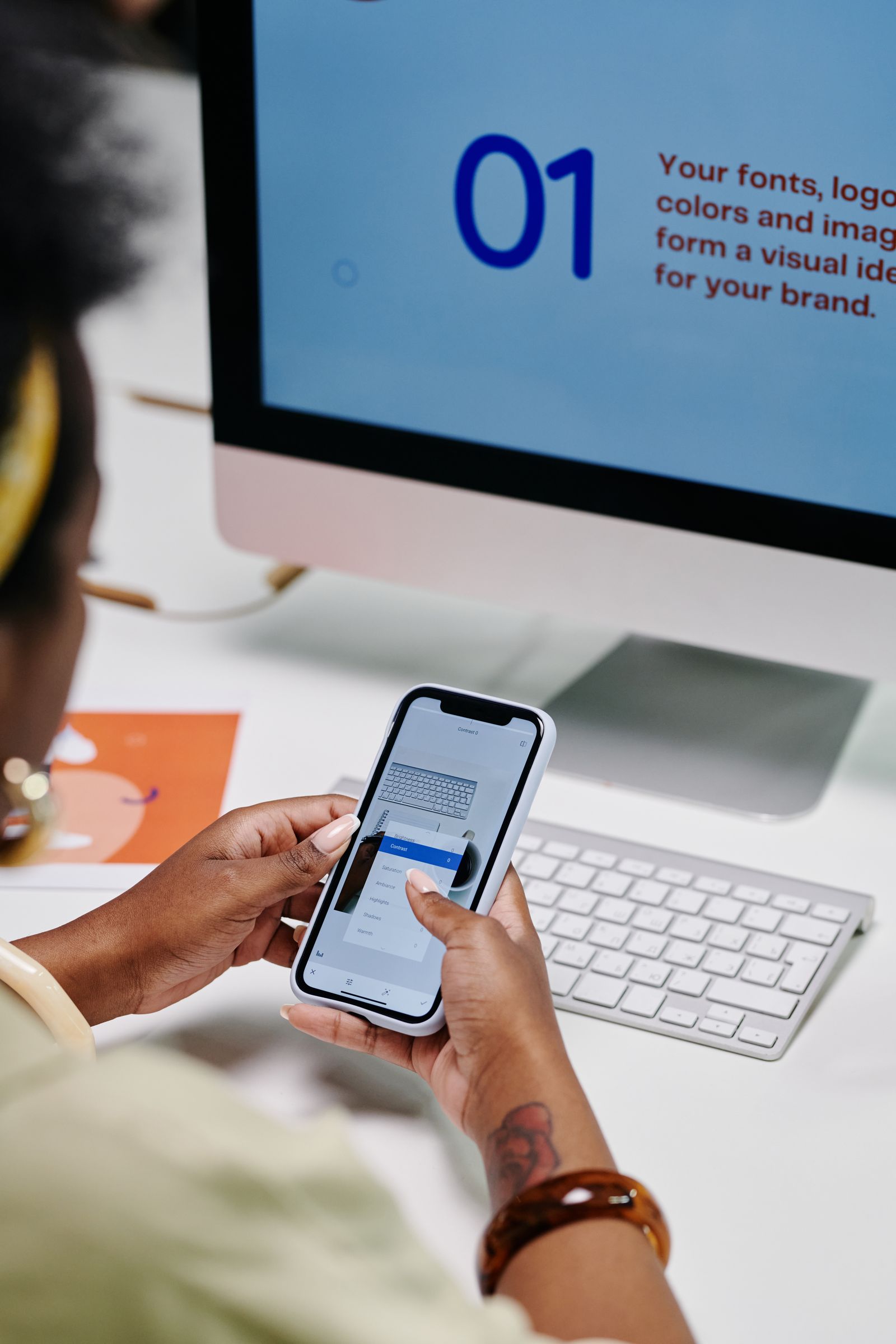 A designer using a smartphone beside a desktop computer